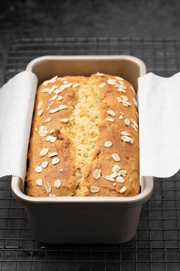 Oat bread baked in loaf pan on white paper on wire rack