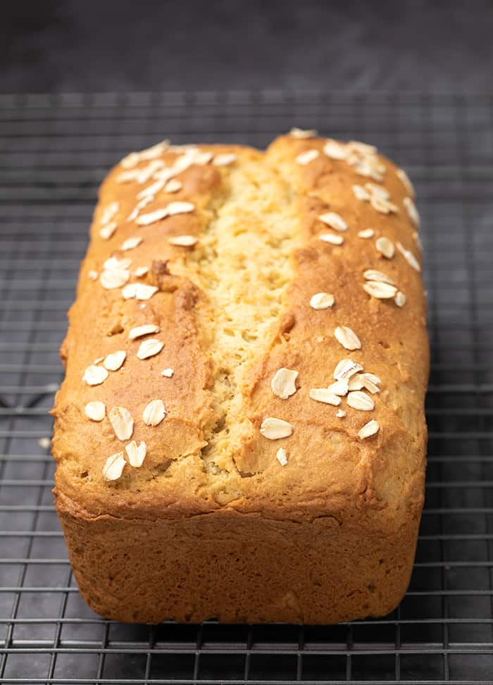 Oat bread with oats on top baked on wire rack on gray surface