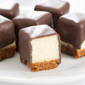 square cheesecake bites with light yellow inside, brown crust and brown chocolate on outside