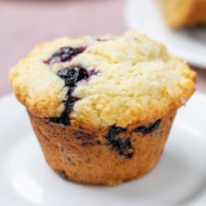 blueberry muffin on small white plate on purple cloth