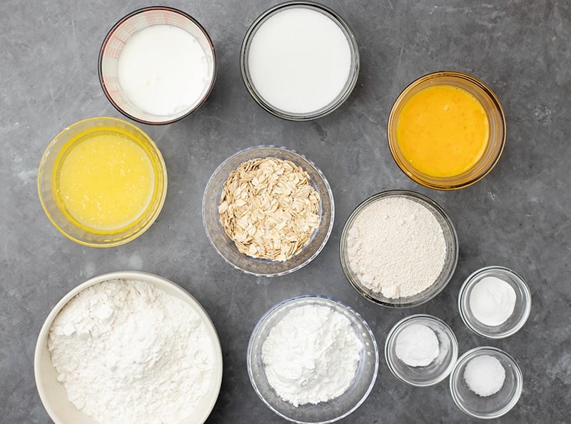 Small glass bowls with white powders, old fashioned oats, white liquids, yellow liquids on gray surface