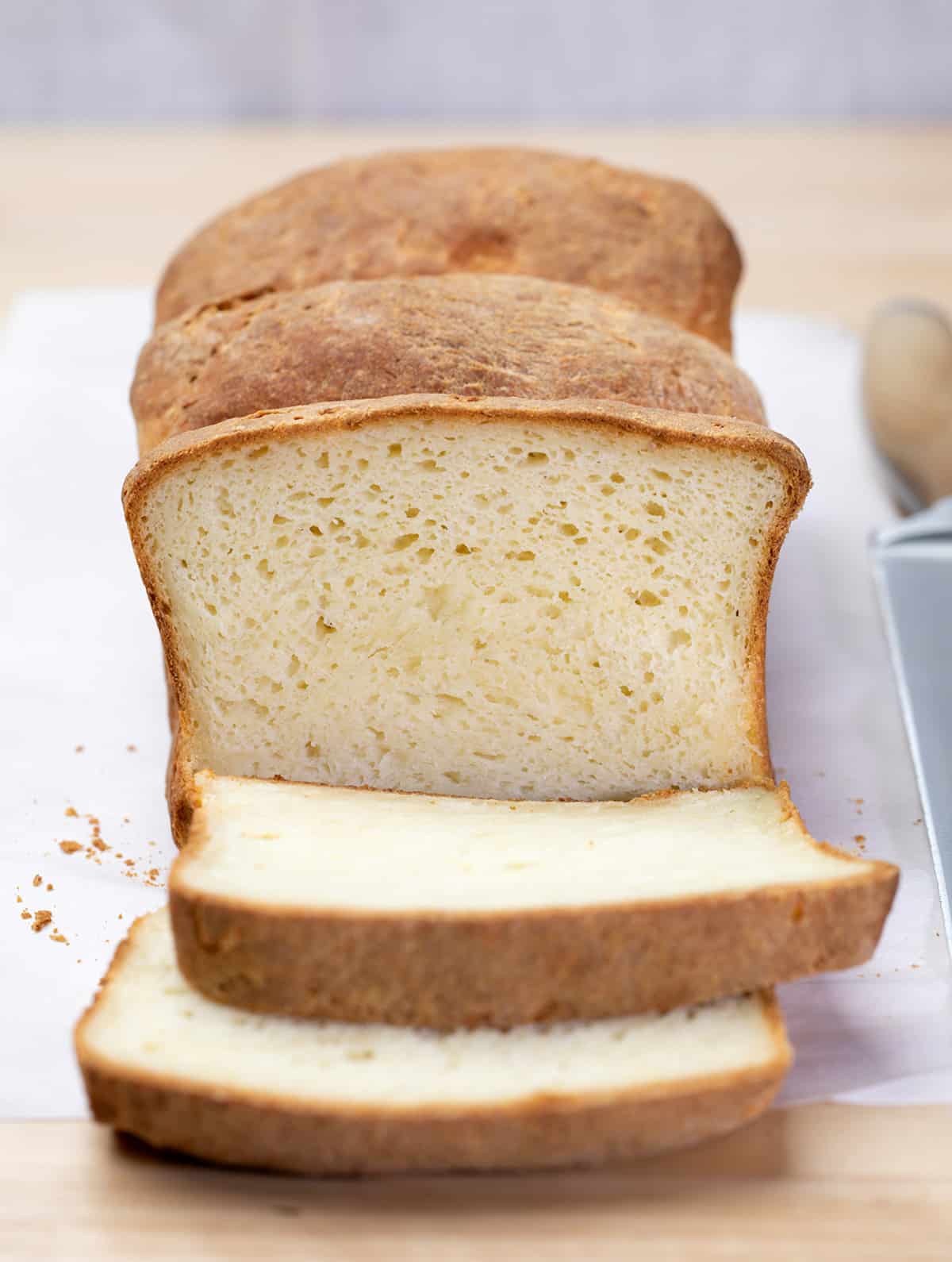 Loaf of bread with 2 slices on white paper with a large bread knife