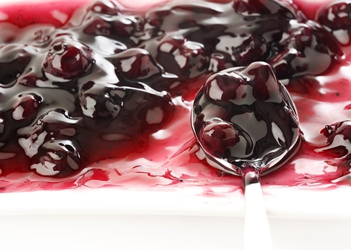 cooked shiny blueberries on a white surface, some on a metal spoon