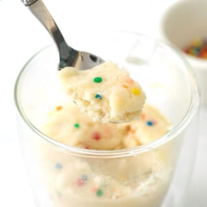 spoon holding spoonful of vanilla mug cake with colored edible confetti pieces over glass mug