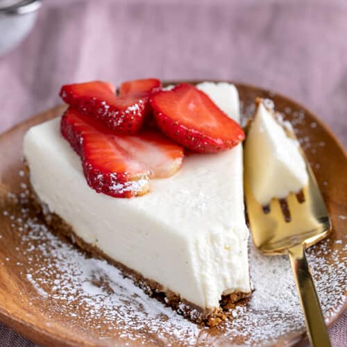 slice of no bake cheesecake with berries and powdered sugar on small brown plate with gold fork