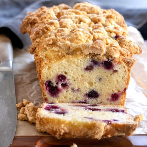 gluten free blueberry bread loaf with one piece sliced on brown paper with large knife