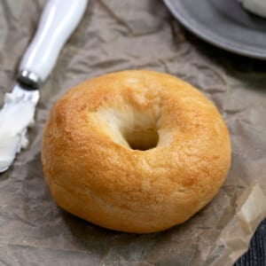 light brown bagel on brown paper with knife with cream cheese