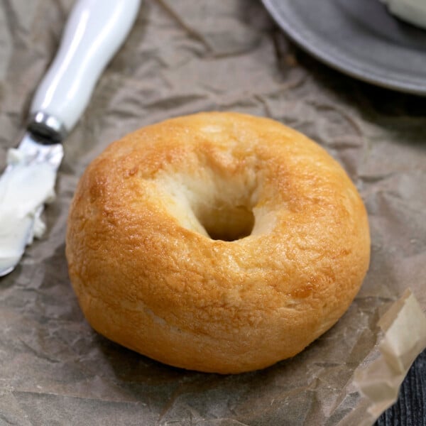 light brown bagel on brown paper with knife with cream cheese