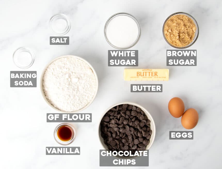 overhead image of gluten free chocolate chip cookies ingredients in round bowls with words printed below each ingredient on light marble surface