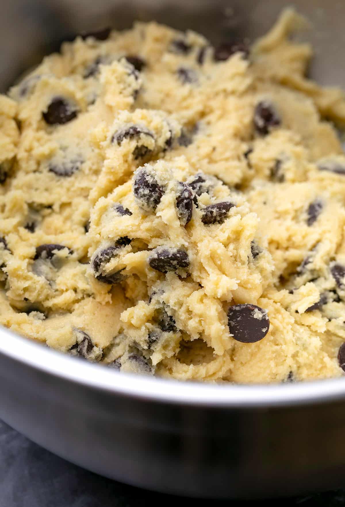 Metal mixing bowl with chocolate chips and thick light brown cookie dough. 