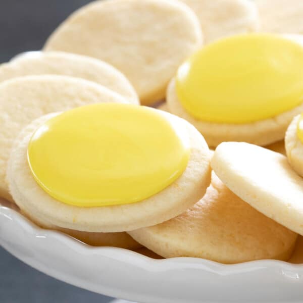 gluten free lemon cookies, some with yellow icing on top, on a white platter with scalloped edge