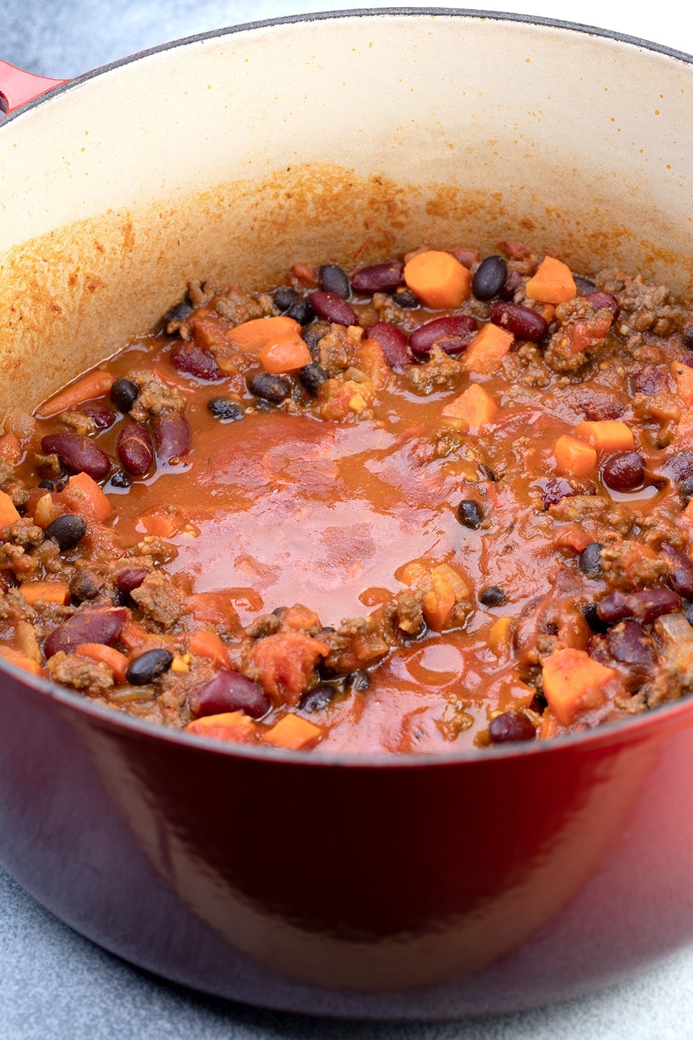 The chili in a red cast iron pot thickened after simmering with cooked carrots, beef and beans.