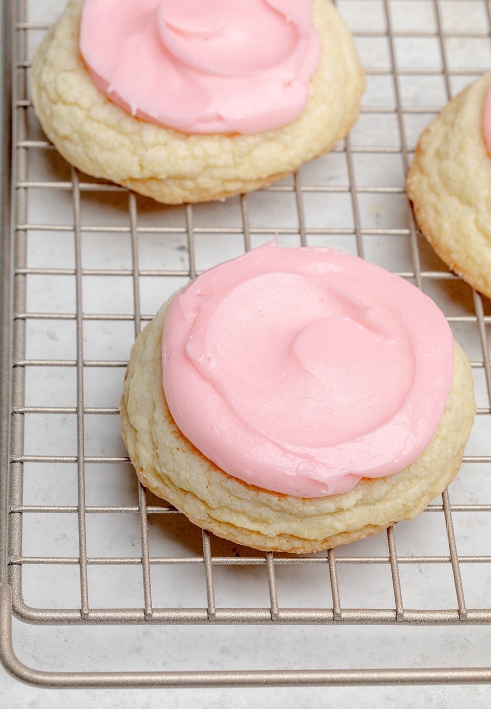 light yellow cookies with pink frosting on wire rack overhead