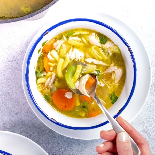 gluten free chicken noodle soup in white bowl with hand holding spoon