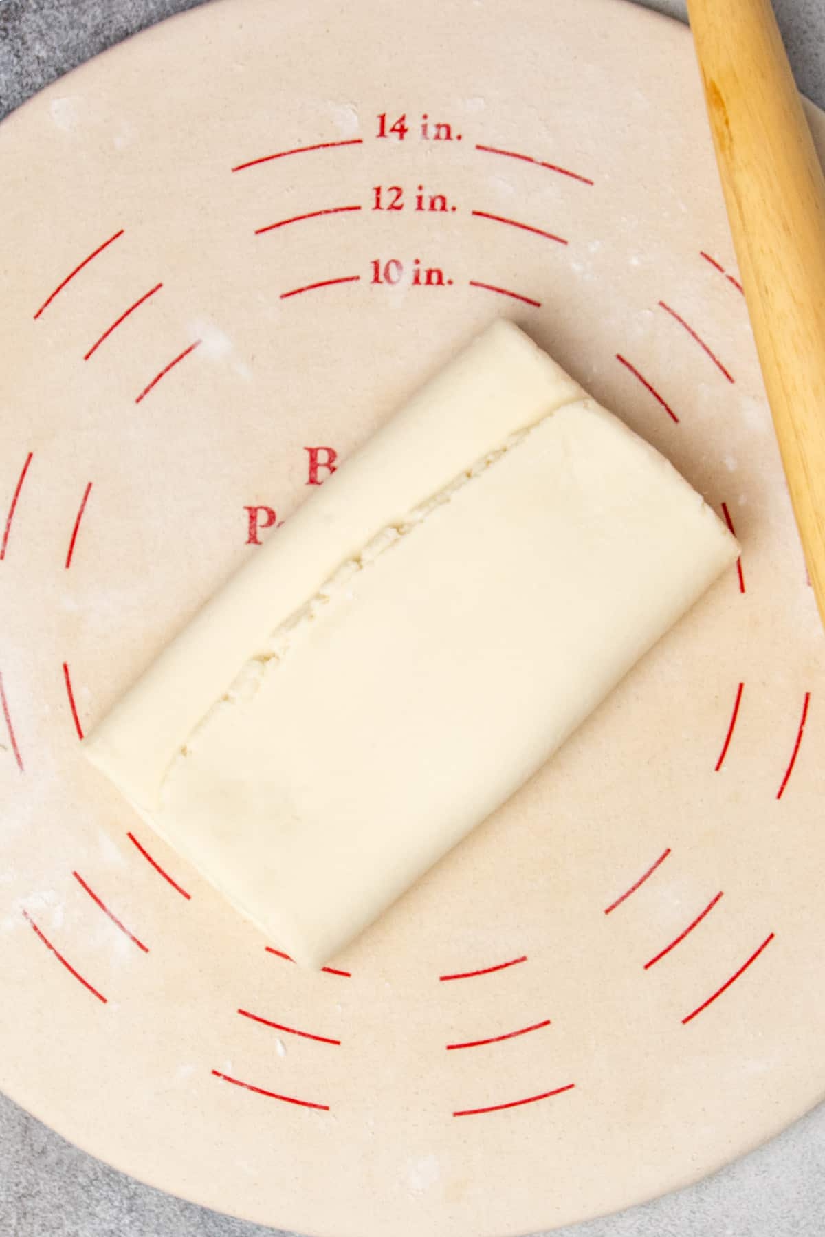 Pastry dough rolled out and folded in thirds like a business letter on light tan pastry board.