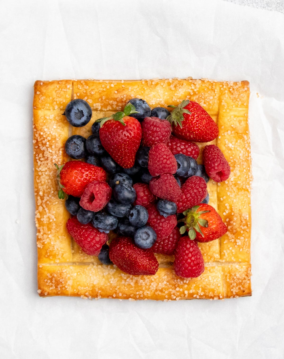 Overhead image of golden brown pastry square with strawberries, blueberries and raspberries in center.