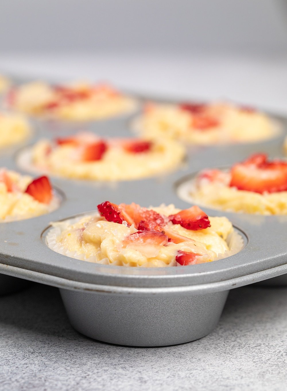 Raw strawberry muffins with chopped strawberries on top in muffin tin.