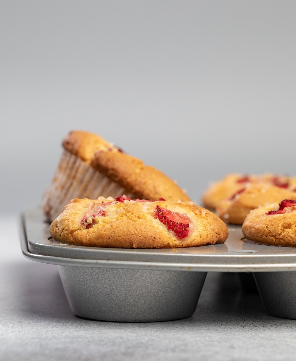 Strawberry muffins in muffin tin with one muffin on its side.