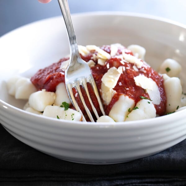 wide white bowl with gluten free potato gnocchi with tomato sauce, shaved cheese, and metal fork