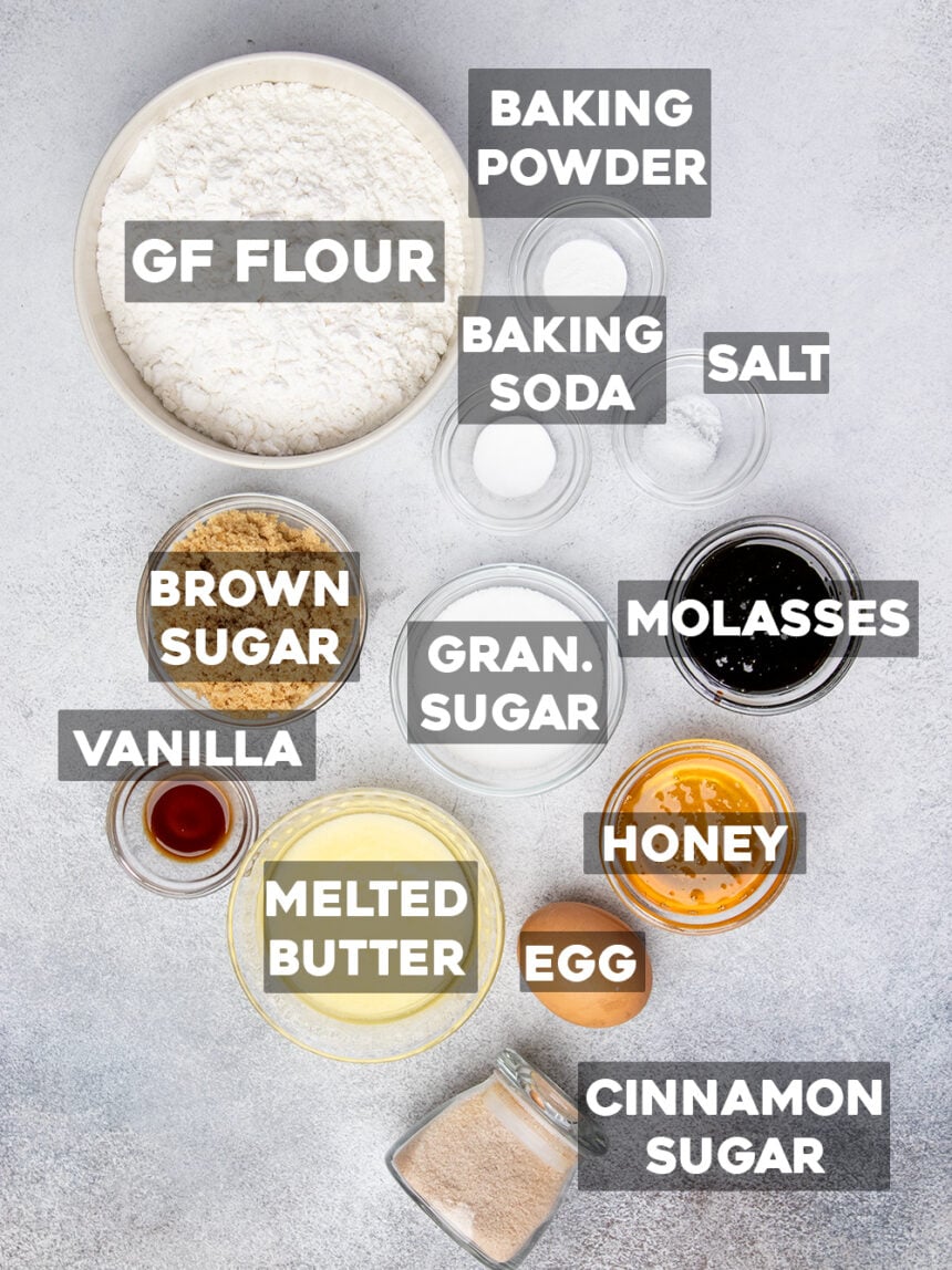 overhead image with the ingredients for gluten free graham crackers with the names of the ingredients written on top: gf flour, baking power, baking soda, salt, gran. sugar, brown sugar, molasses, melted butter, honey, egg, and cinnamon sugar