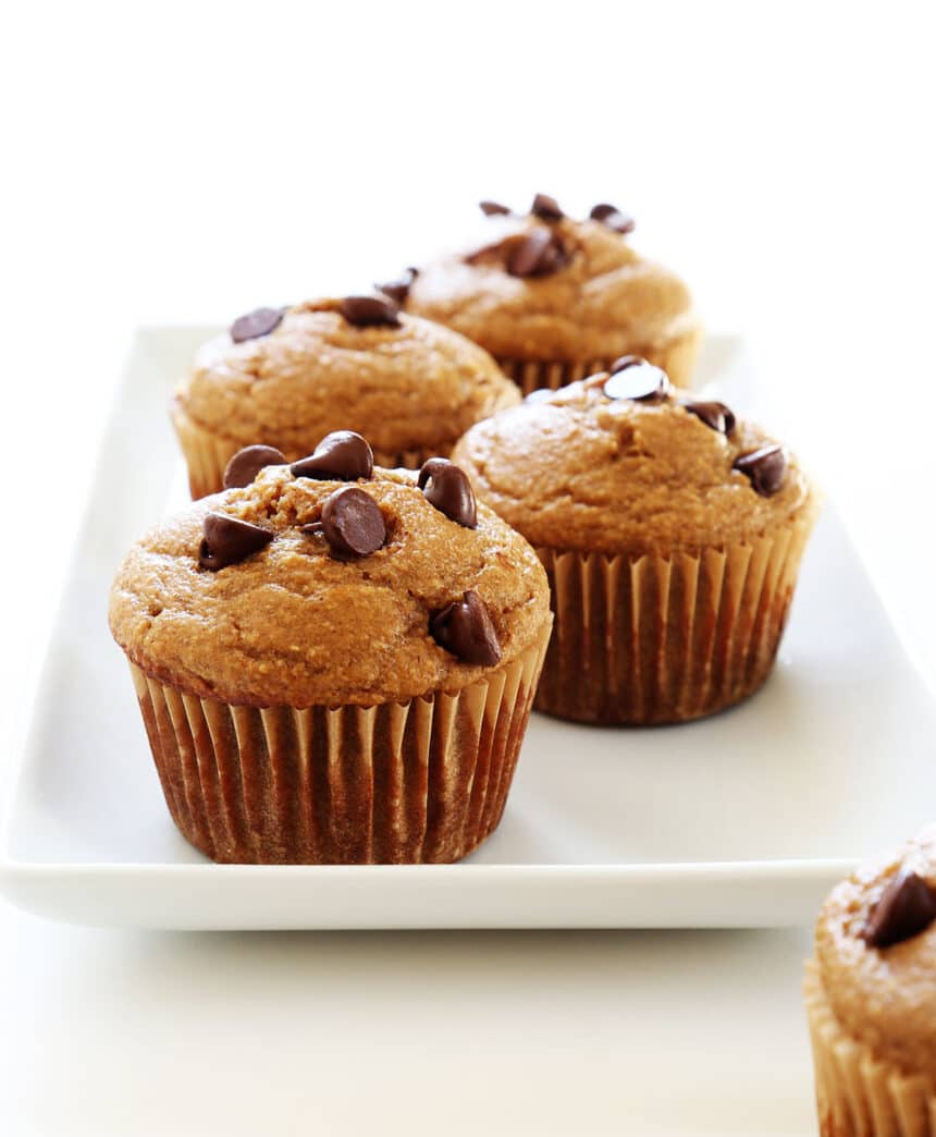 4 brown banana oatmeal muffins with chocolate chips on top in brown paper on rectangular white tray