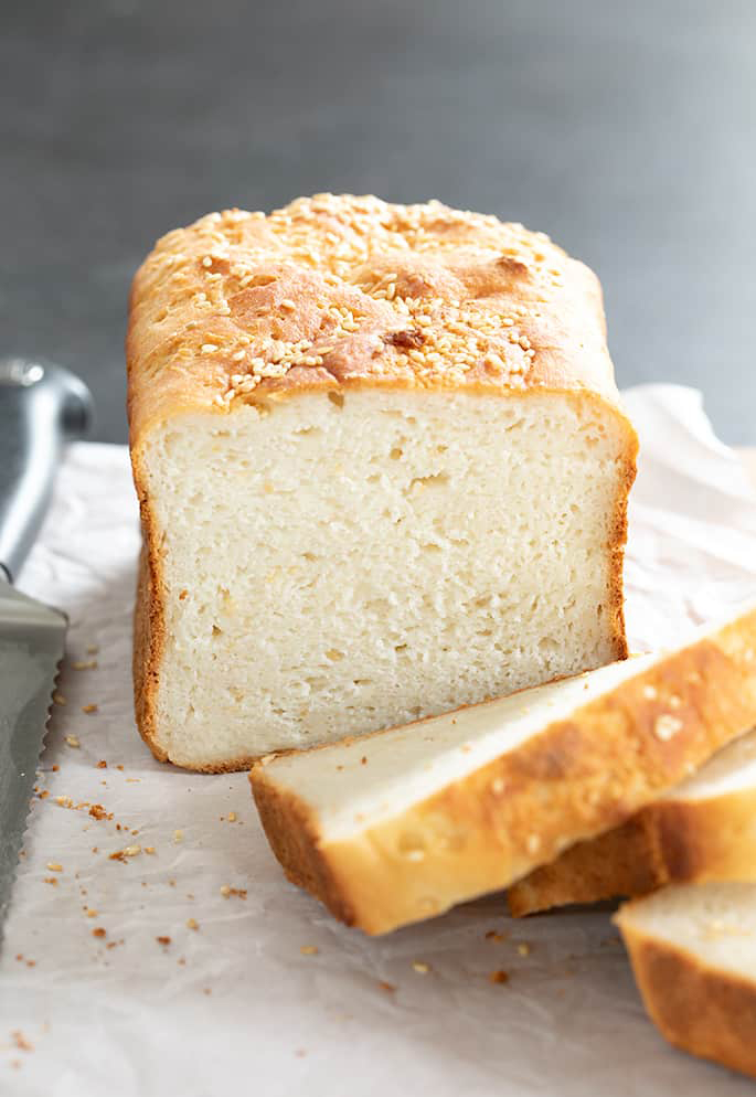 Bread made with gluten free bread recipe with seeds sliced on white paper sitting on cutting board