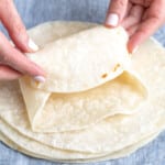 hands folding gluten free tortilla on top of stack