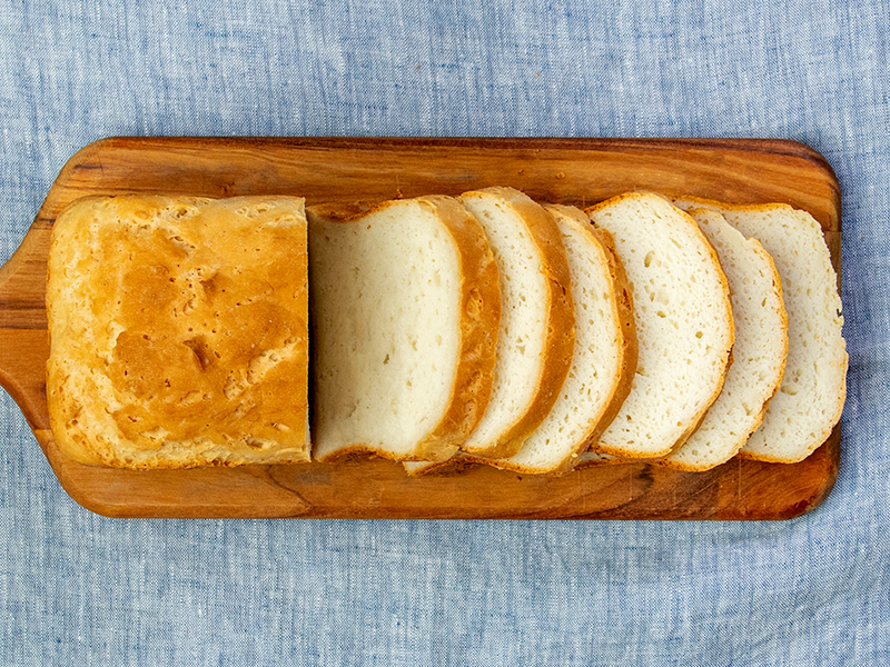 Horizontal image of partially sliced bread recipe on wood board on blue cloth