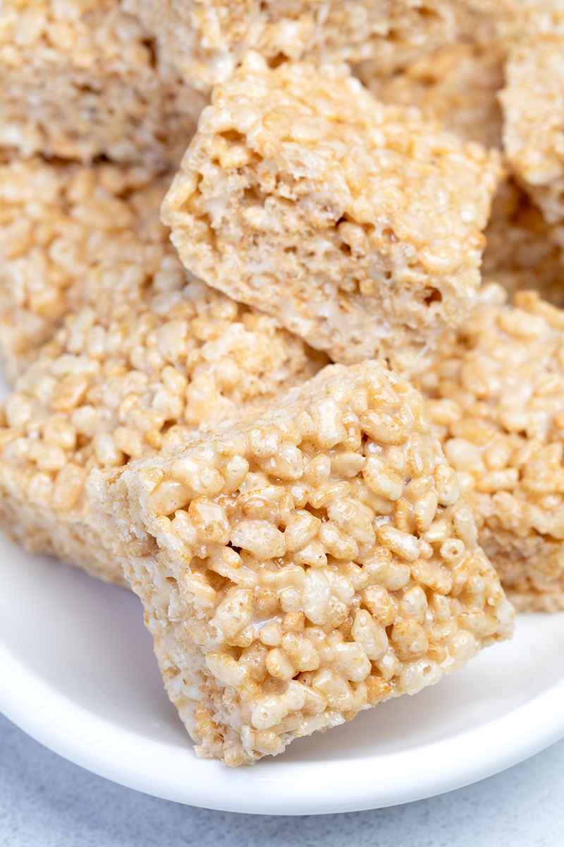 Closeup image of square gluten free rice krispie treats on edge of white oval serving dish