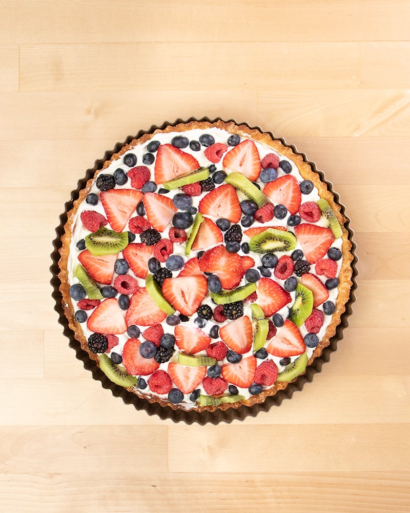 Overhead image of round tart pan with fruit tart with sliced strawberries, blackberries, blueberries, sliced kiwi.