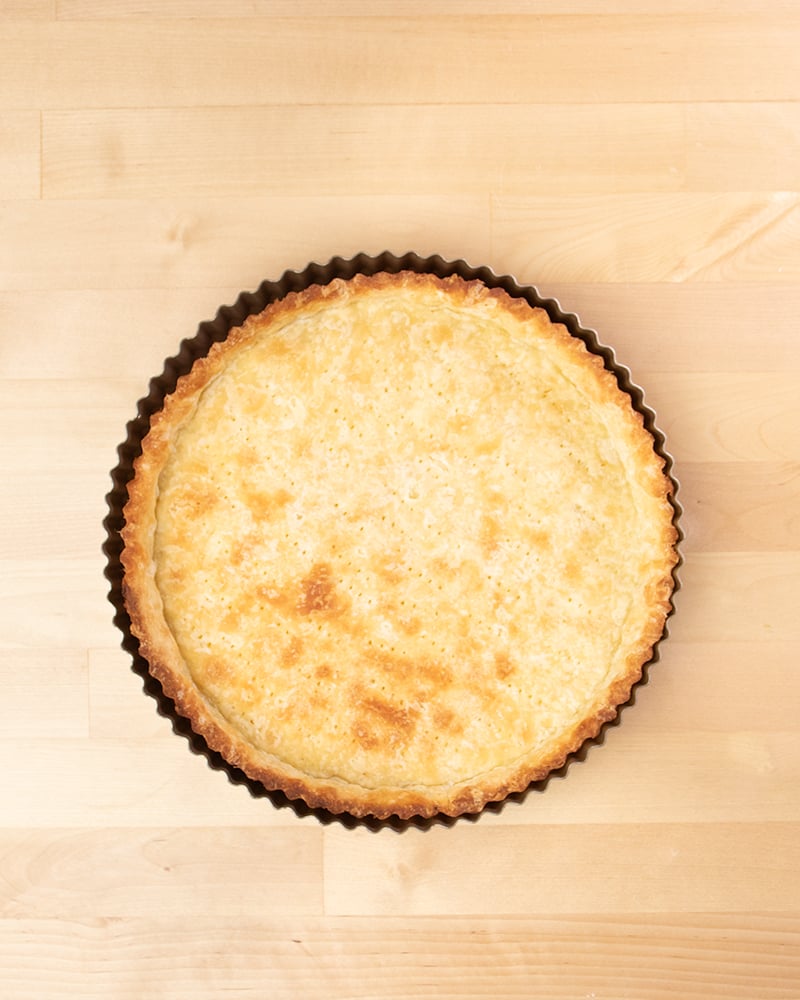 Overhead image of round tart pan with light brown baked gluten free shortcrust pastry tart