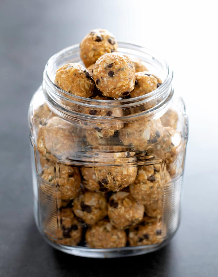 light brown oat protein balls with mini chocolate chips in large glass jar on black counter