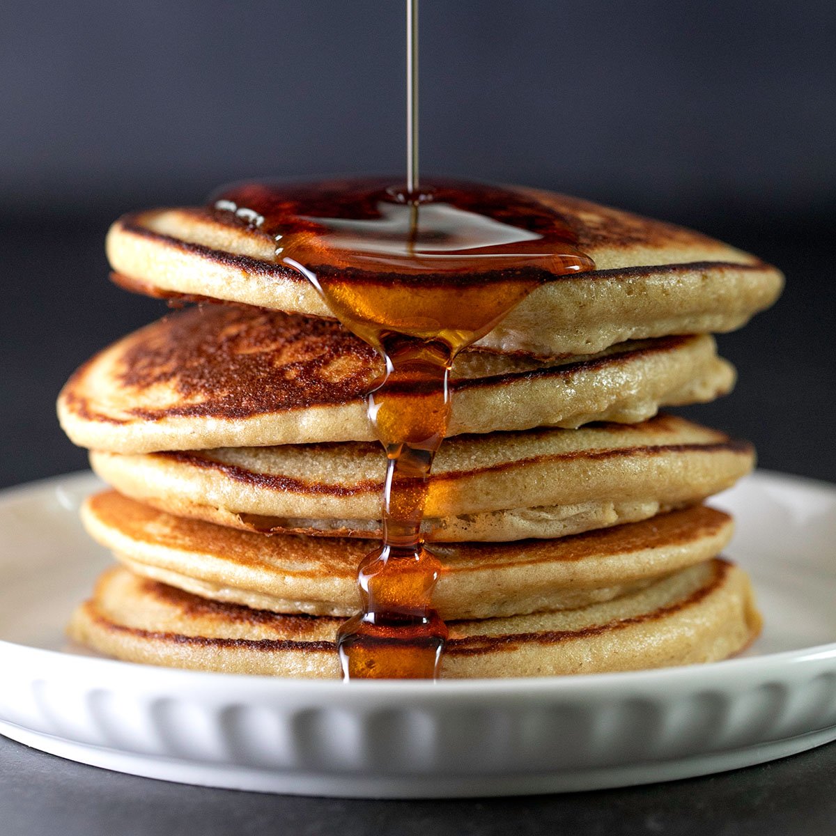 stack of 6 gluten free protein pancakes with syrup pouring on white plate