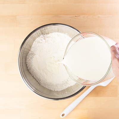 Pouring milk from measuring cup into pancake dry mix in bowl