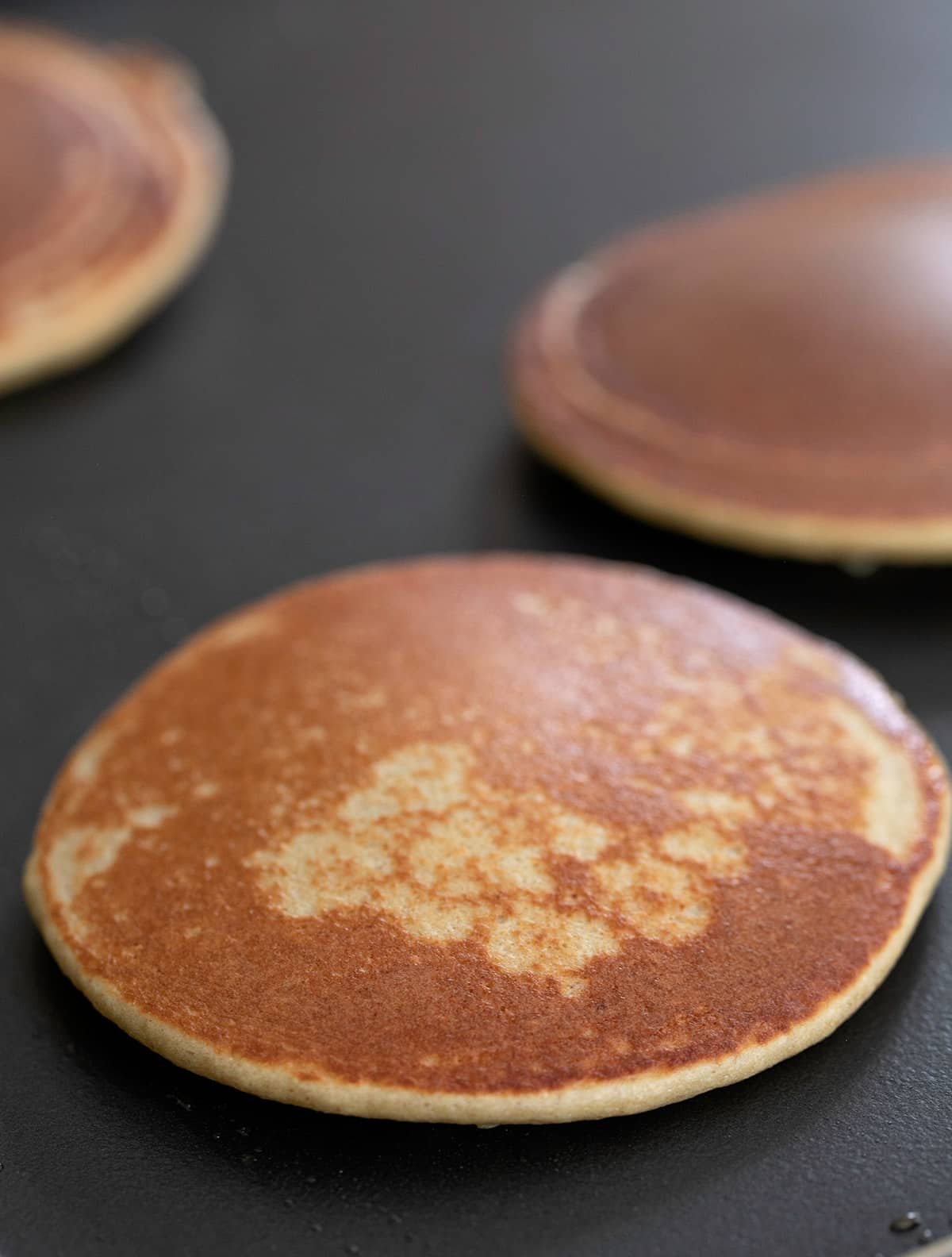 Protein pancake cooking on griddle with cooked side up