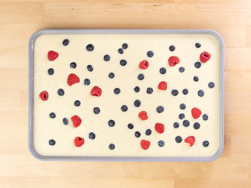 Raw sheet pan pancake batter with red and blue berries on top