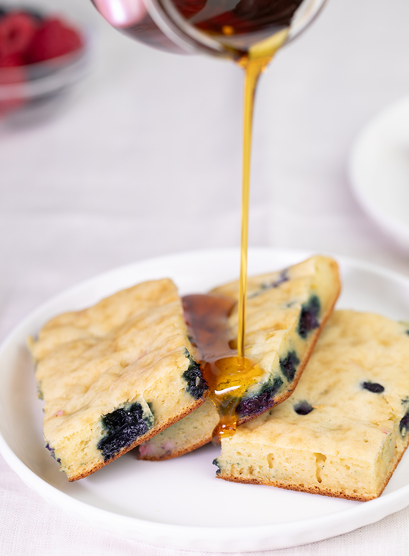 Syrup pouring onto white plate with 3 slices of sheet pan pancake