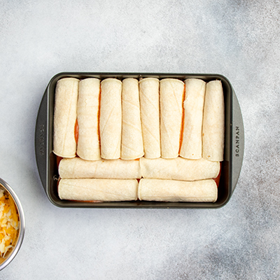 12 filled corn tortillas in black casserole dish