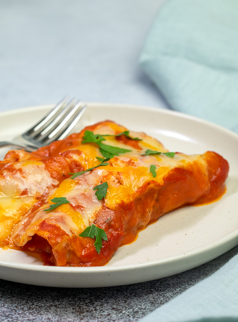 2 gluten free enchiladas with parsley on plate with fork