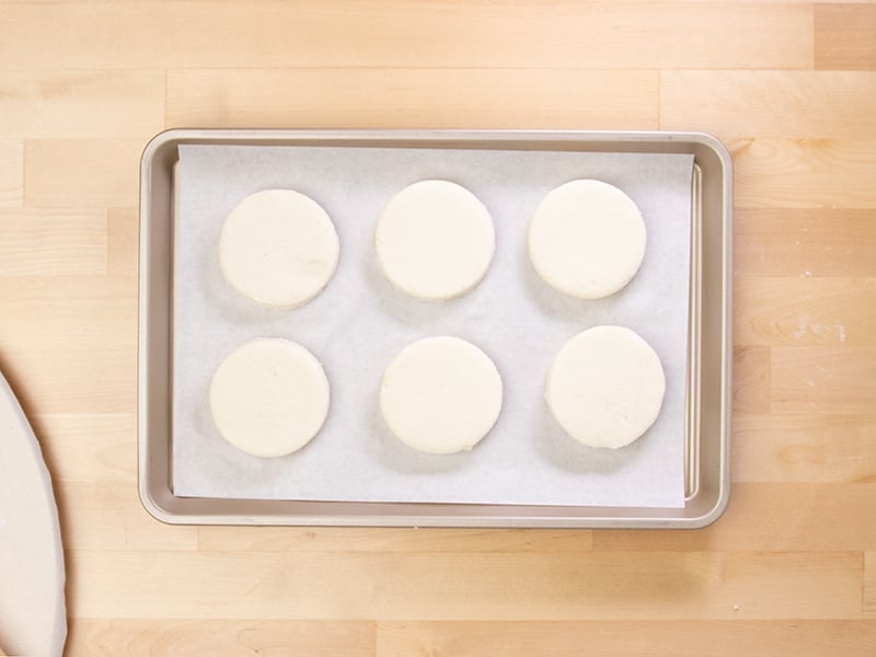 6 rounds of raw gluten free biscuits on white paper on baking tray