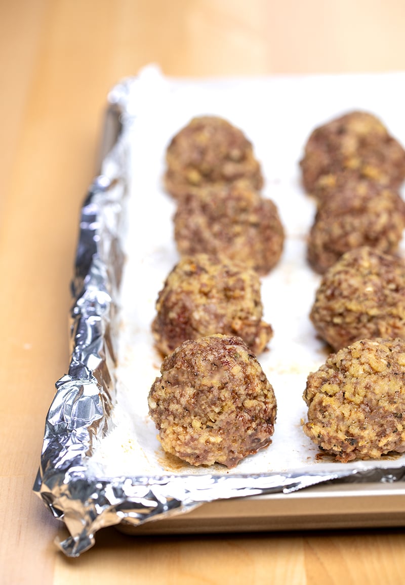 8 baked meatballs on white paper on foil-lined baking tray