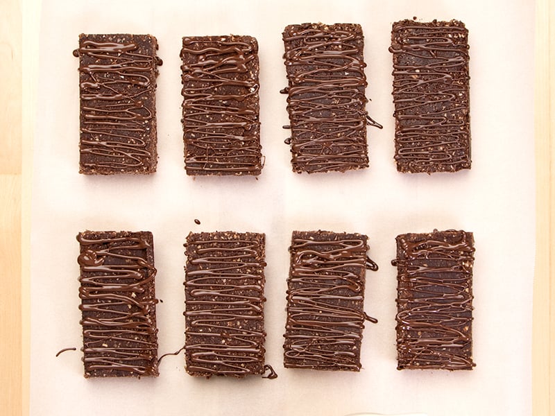 8 brown protein bars with chocolate drizzle on top on white paper