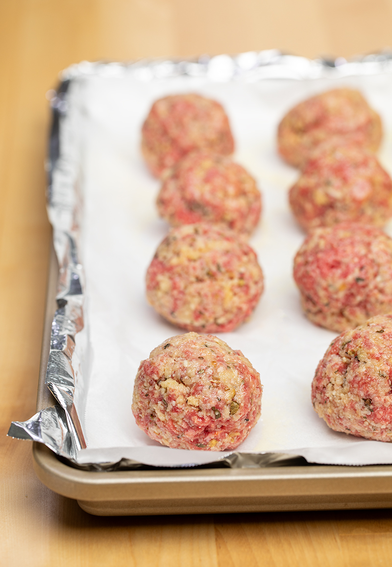 8 raw meatballs on white paper and foil on tray