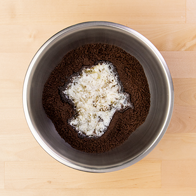 Chocolate cookie crumbs and melted butter in small round metal bowl