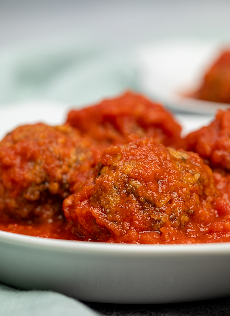 Closeup of 4 meatballs with tomato sauce in white dish with blue cloth