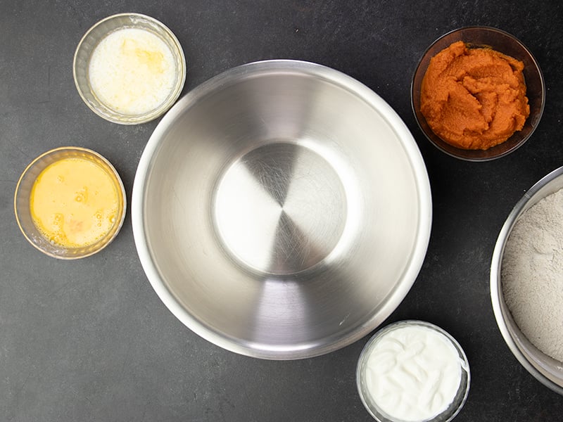 Empty metal mixing bowl with small bowls with beaten eggs, melted butter, sour cream