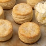 closeup image of 3 whole and 3 partial round layered and golden brown biscuits on baking paper with butter