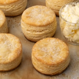 closeup image of 3 whole and 3 partial round layered and golden brown biscuits on baking paper with butter