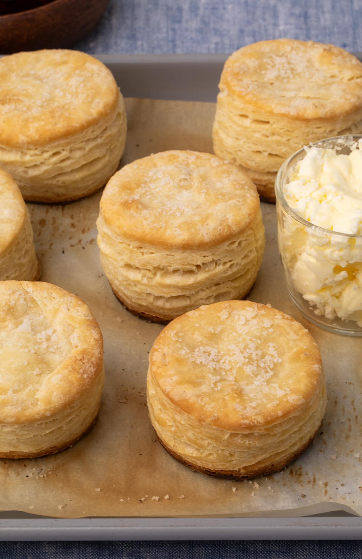 6 golden brown, round layered and flaky gluten free biscuits on browned parchment on a gray baking tray