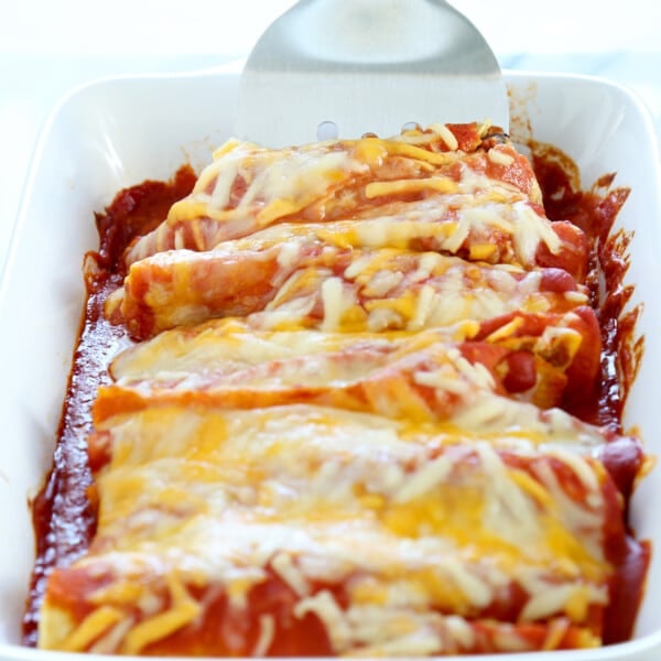 spatula lifting enchiladas from white casserole dish